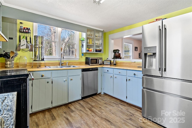 kitchen with appliances with stainless steel finishes, light countertops, a textured ceiling, light wood-style floors, and a sink