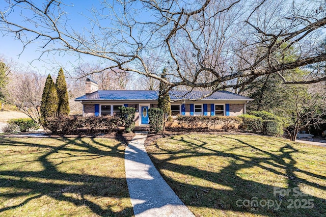 view of front of property featuring metal roof, brick siding, a front lawn, and a chimney