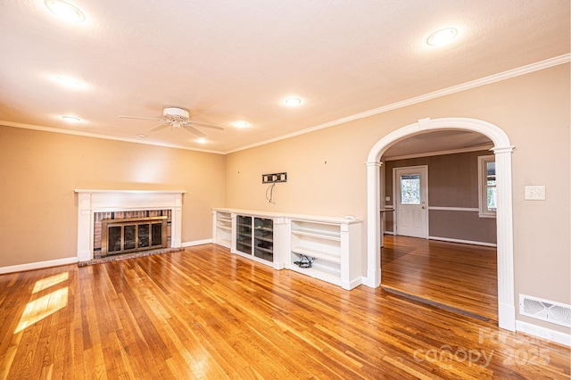 unfurnished living room featuring arched walkways, crown molding, visible vents, a ceiling fan, and wood finished floors