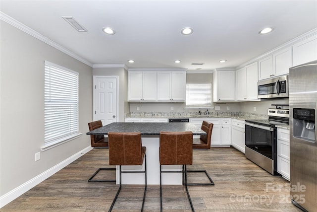 kitchen with a center island, a breakfast bar, stainless steel appliances, visible vents, and white cabinets