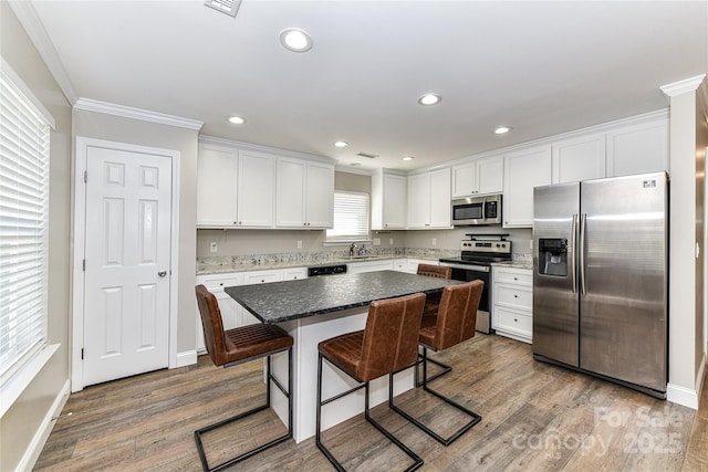 kitchen with wood finished floors, a center island, stainless steel appliances, a kitchen bar, and white cabinetry