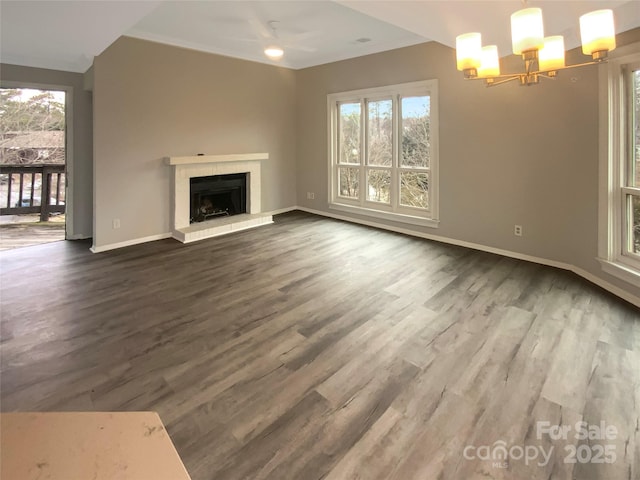 unfurnished living room featuring hardwood / wood-style floors, a wealth of natural light, a tiled fireplace, and a chandelier