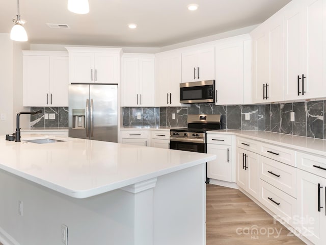 kitchen featuring appliances with stainless steel finishes, decorative light fixtures, white cabinetry, sink, and light wood-type flooring