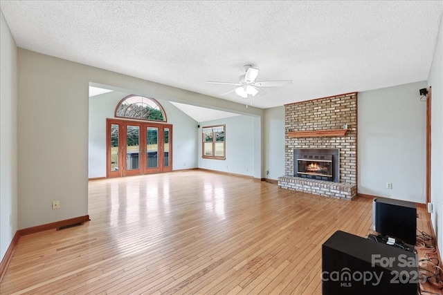 unfurnished living room with lofted ceiling, ceiling fan, a textured ceiling, a brick fireplace, and light wood-type flooring