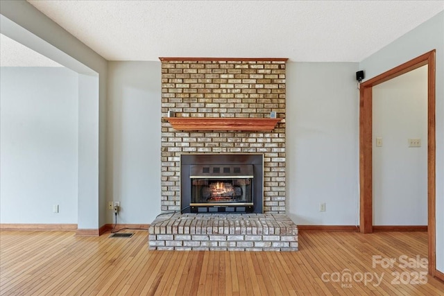 unfurnished living room featuring a brick fireplace, wood-type flooring, and a textured ceiling