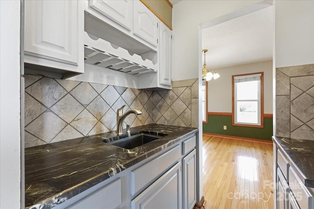 kitchen with pendant lighting, sink, white cabinetry, tasteful backsplash, and light hardwood / wood-style floors