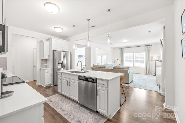 kitchen with stainless steel appliances, a sink, white cabinetry, decorative backsplash, and a center island with sink