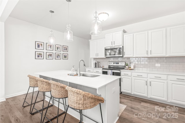 kitchen featuring stainless steel appliances, wood finished floors, a sink, light countertops, and tasteful backsplash