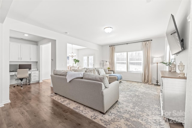 living area with built in study area, a notable chandelier, baseboards, and wood finished floors