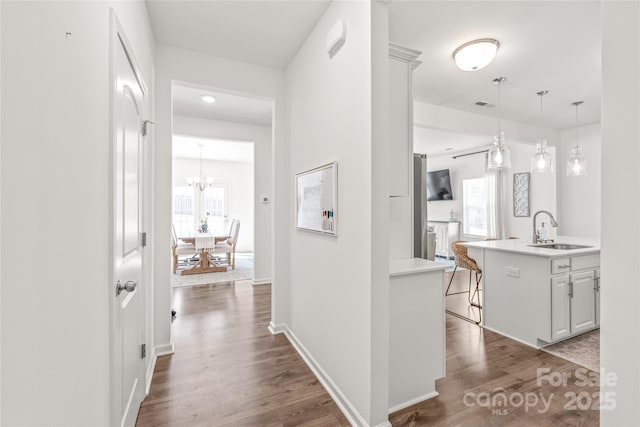 hall featuring visible vents, a sink, dark wood finished floors, and baseboards