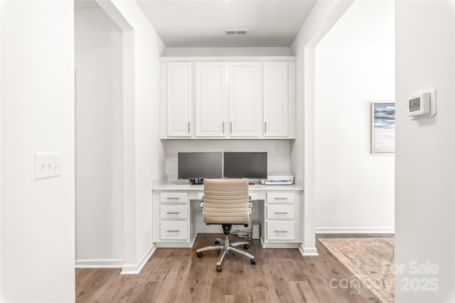 home office featuring light wood-style flooring, visible vents, baseboards, and built in study area