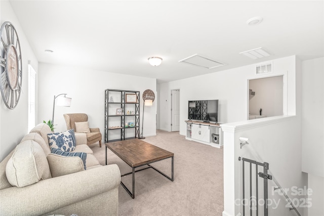 living area with attic access, visible vents, baseboards, and light colored carpet