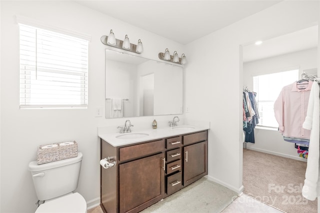 bathroom featuring toilet, double vanity, baseboards, and a sink