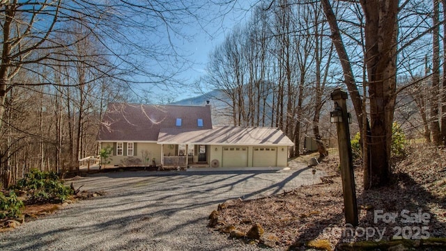 cape cod home featuring aphalt driveway, a porch, a chimney, and an attached garage