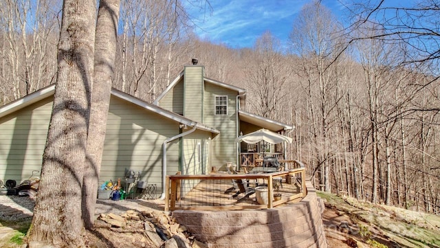 rear view of property with a wooded view, a chimney, and a wooden deck