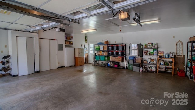 garage with a garage door opener, freestanding refrigerator, and electric panel