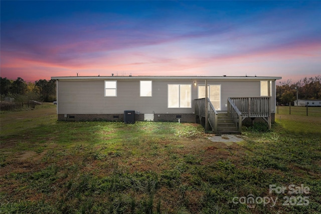 back house at dusk with central AC unit, a yard, and a deck