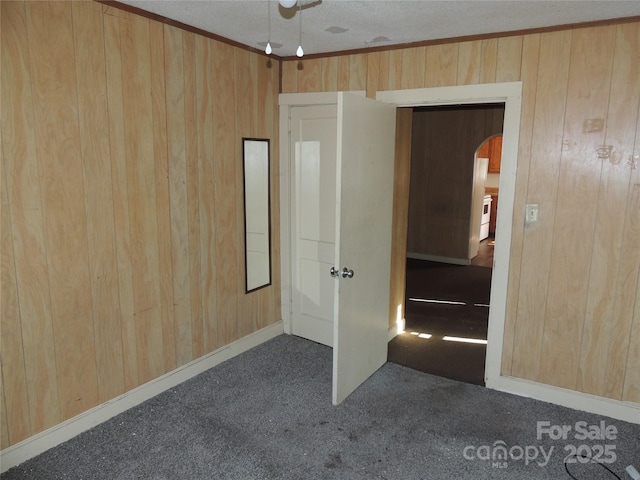 empty room with ornamental molding, dark colored carpet, and wooden walls