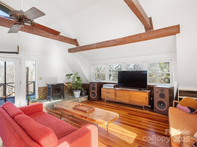 living room with beam ceiling, hardwood / wood-style flooring, plenty of natural light, and a wood stove