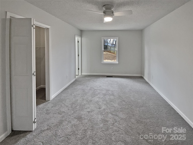 unfurnished bedroom with ceiling fan, carpet floors, a textured ceiling, and a spacious closet