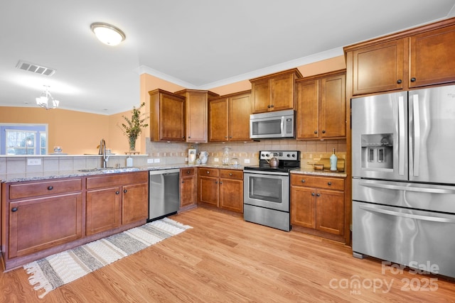 kitchen featuring tasteful backsplash, sink, light hardwood / wood-style floors, stainless steel appliances, and light stone countertops