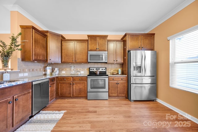 kitchen featuring light stone counters, stainless steel appliances, light hardwood / wood-style flooring, and backsplash