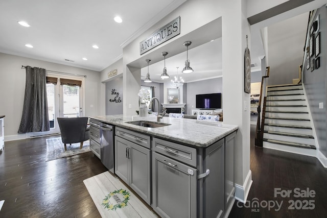 kitchen with pendant lighting, gray cabinets, a sink, an island with sink, and light stone countertops