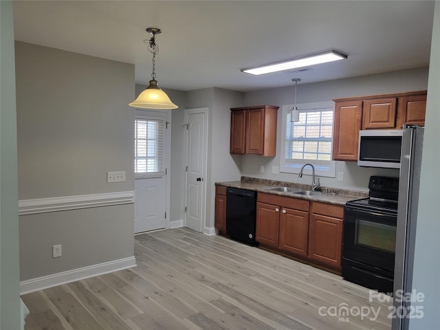 kitchen featuring black appliances, light wood finished floors, a sink, and decorative light fixtures