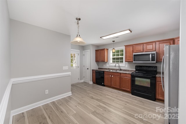 kitchen with hanging light fixtures, a sink, light wood-style flooring, baseboards, and black appliances