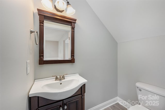 half bathroom with vanity, wood finished floors, toilet, baseboards, and vaulted ceiling