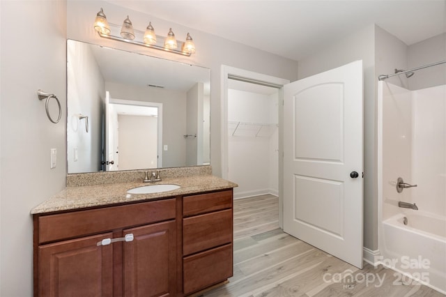 bathroom featuring a spacious closet, tub / shower combination, wood finished floors, and vanity