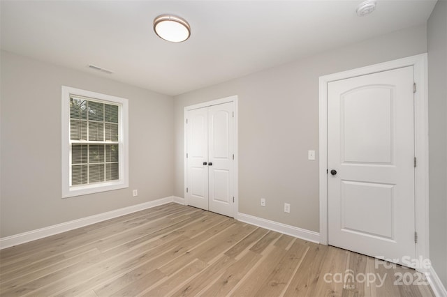 unfurnished bedroom featuring baseboards, a closet, light wood-type flooring, and visible vents