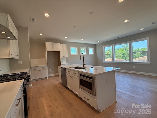 kitchen featuring an island with sink, white cabinetry, a sink, light wood-style flooring, and stainless steel appliances