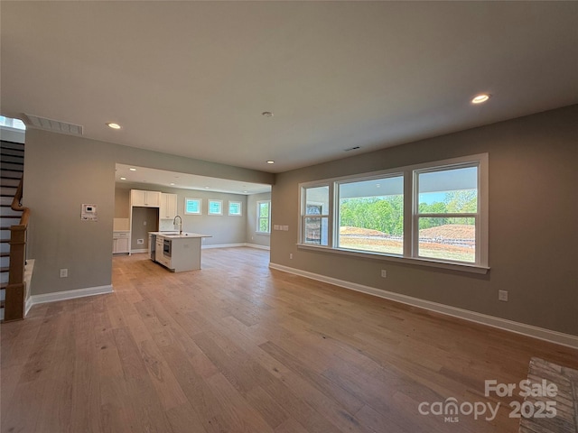 unfurnished living room featuring light wood-type flooring, a sink, baseboards, stairway, and recessed lighting
