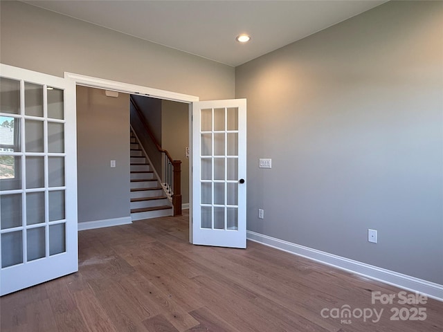 unfurnished room featuring french doors, stairs, baseboards, and wood finished floors