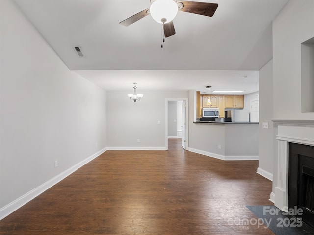 unfurnished living room featuring ceiling fan with notable chandelier, dark wood-style flooring, a fireplace with flush hearth, visible vents, and baseboards