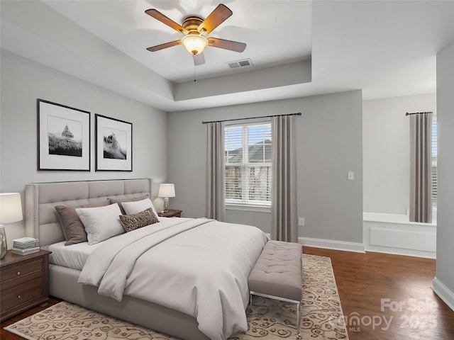 bedroom with baseboards, visible vents, dark wood-style floors, ceiling fan, and a tray ceiling