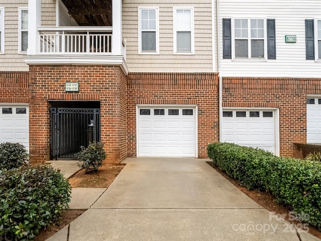 view of front of house with a garage, driveway, brick siding, and a balcony