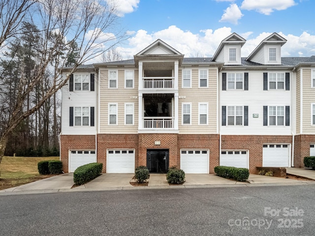 townhome / multi-family property featuring driveway, brick siding, an attached garage, and a balcony