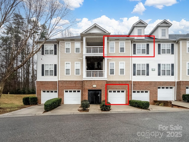 multi unit property featuring a garage, brick siding, driveway, and a balcony