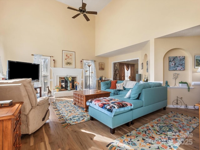 living room featuring hardwood / wood-style flooring, ceiling fan, a tile fireplace, and a high ceiling