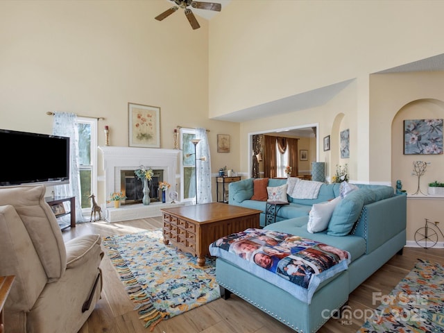 living room featuring ceiling fan, a fireplace, light hardwood / wood-style floors, and a high ceiling