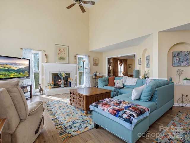 living room featuring ceiling fan, a towering ceiling, and light wood-type flooring