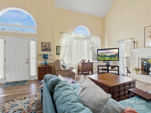 living room with wood-type flooring, high vaulted ceiling, and a brick fireplace