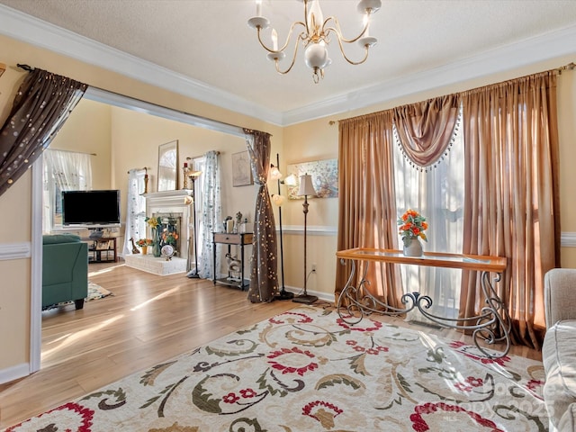 sitting room featuring a fireplace, light wood-type flooring, a notable chandelier, crown molding, and a textured ceiling