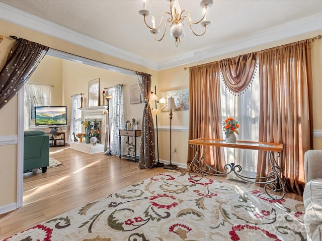 sitting room featuring a tile fireplace, a chandelier, light hardwood / wood-style floors, crown molding, and a textured ceiling