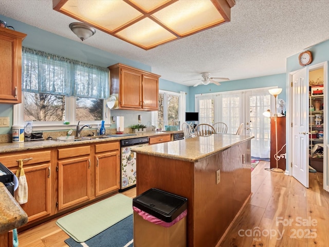 kitchen featuring sink, dishwasher, light stone counters, light hardwood / wood-style floors, and a kitchen island