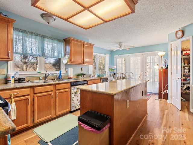 kitchen with sink, a center island, light stone countertops, stainless steel dishwasher, and light wood-type flooring