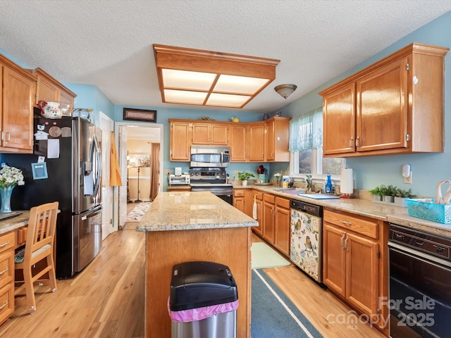 kitchen with a kitchen island, sink, stainless steel appliances, a textured ceiling, and light hardwood / wood-style flooring