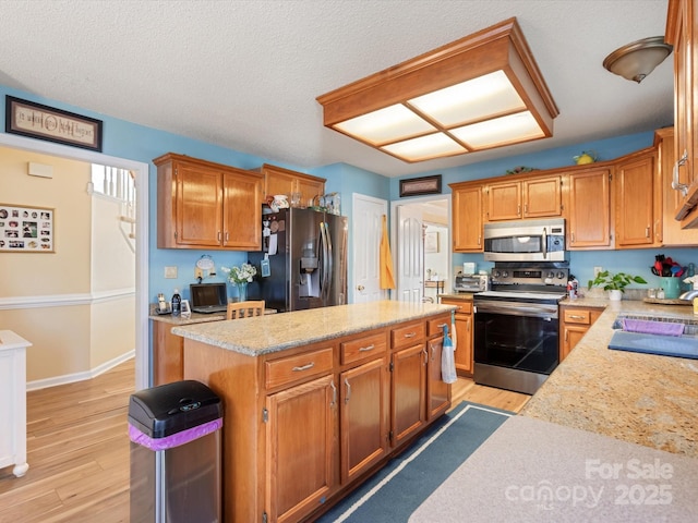 kitchen with sink, appliances with stainless steel finishes, a center island, light hardwood / wood-style floors, and light stone countertops